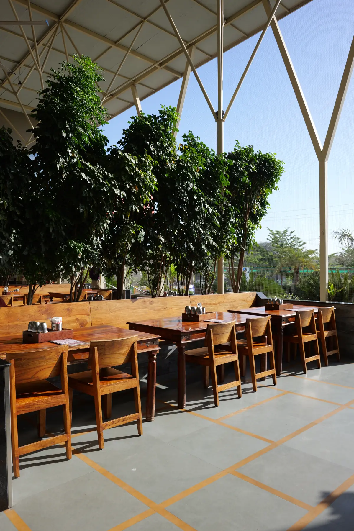 Wooden dining tables under shady trees with garden views